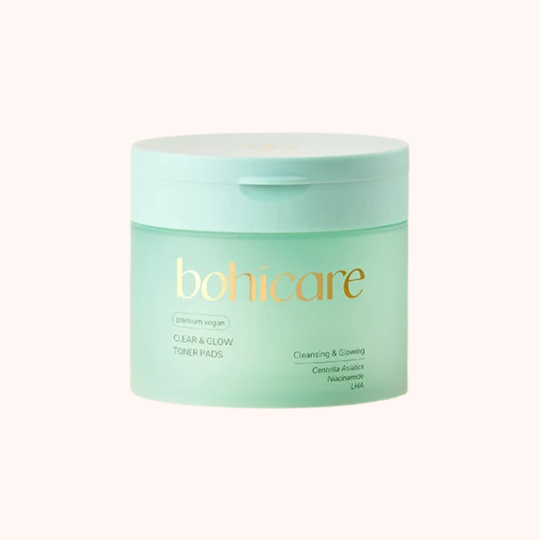 A mint green jar of bohicare Clear &amp; Glow Toner Pads with gold lettering, set against a solid pale pink background.