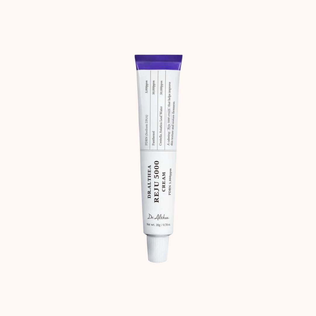A white squeeze tube of Dr. Alhama Healing Repair Cream with a purple cap, centered on a solid pale pink background.