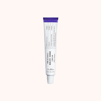 A white squeeze tube of Dr. Alhama Healing Repair Cream with a purple cap, centered on a solid pale pink background.
