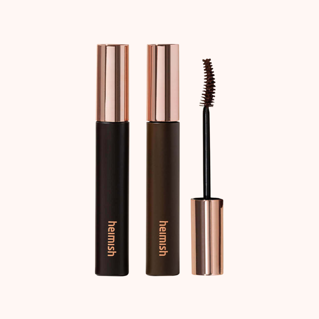 Two tubes of HEMISH mascara with rose gold caps and black bodies, alongside a spoolie wand, on a solid off-white background.
